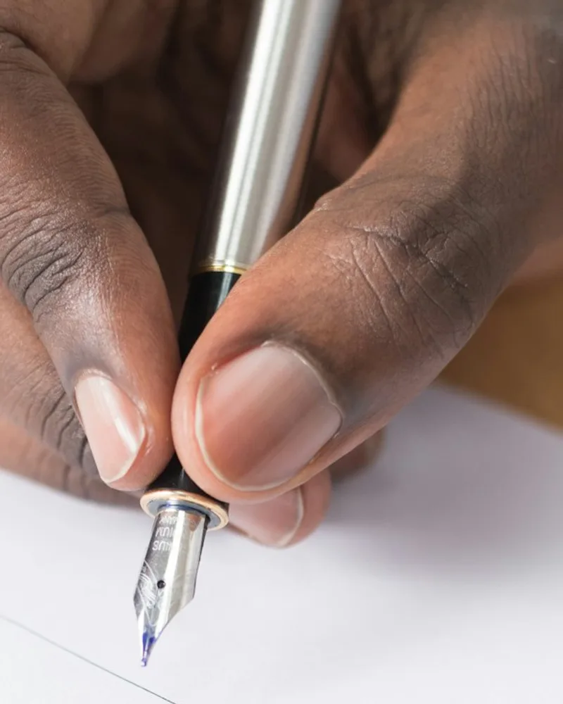 Mão a segurar uma caneta de tinta permanente, pronta a assinar uma folha de papel